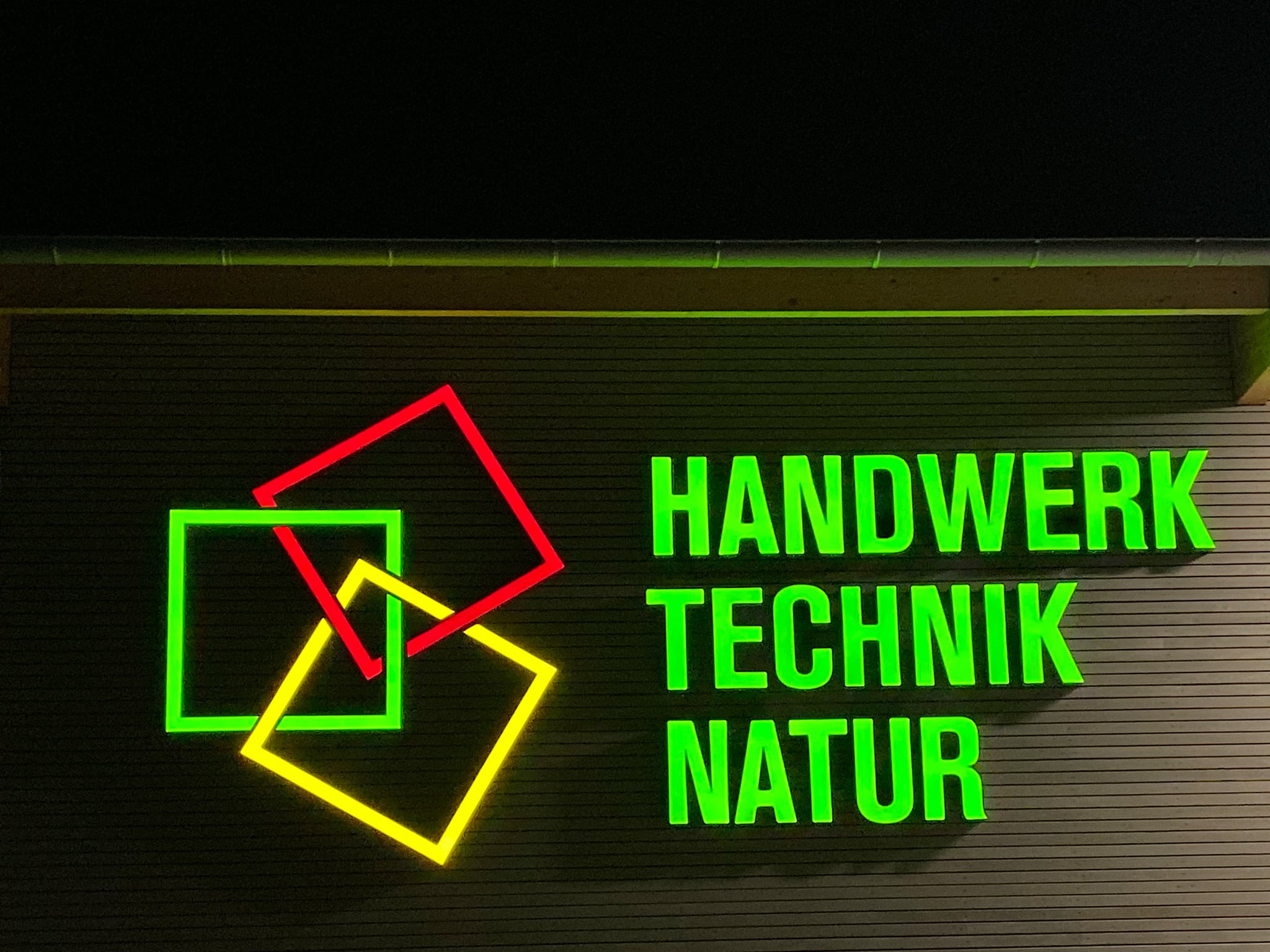 Leuchtreklame „Handwerk Technik Natur“ an einer Fassade
