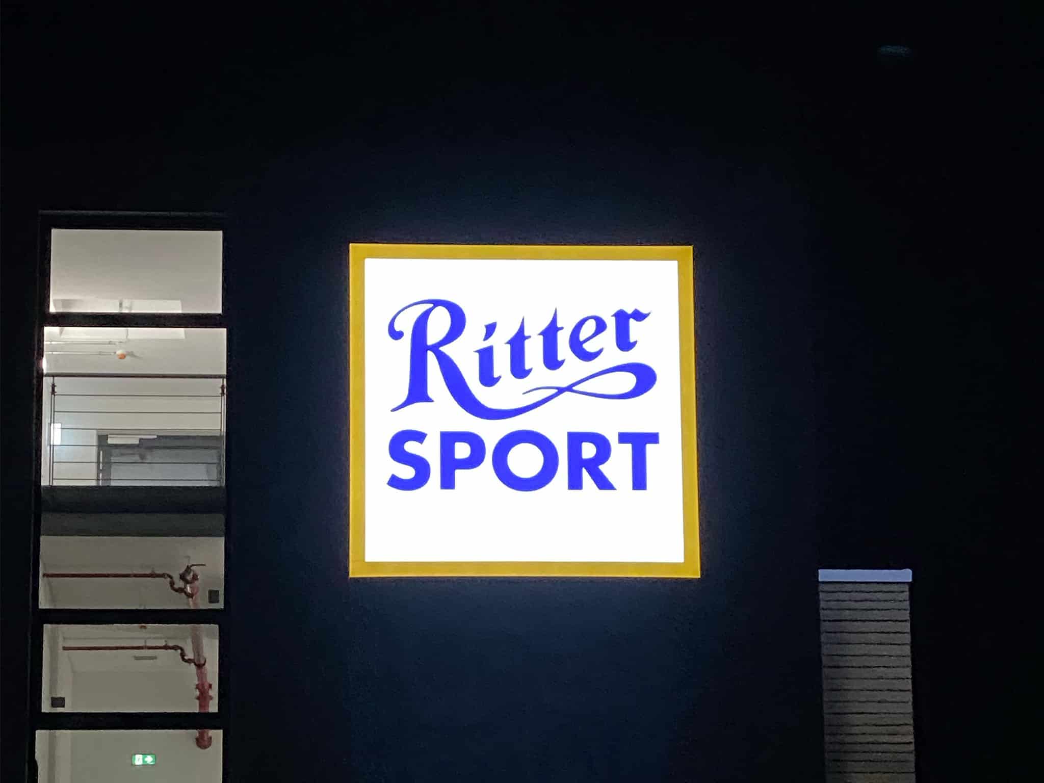 Beleuchtetes Ritter-Sport-Logo an einer Fassade bei Nacht