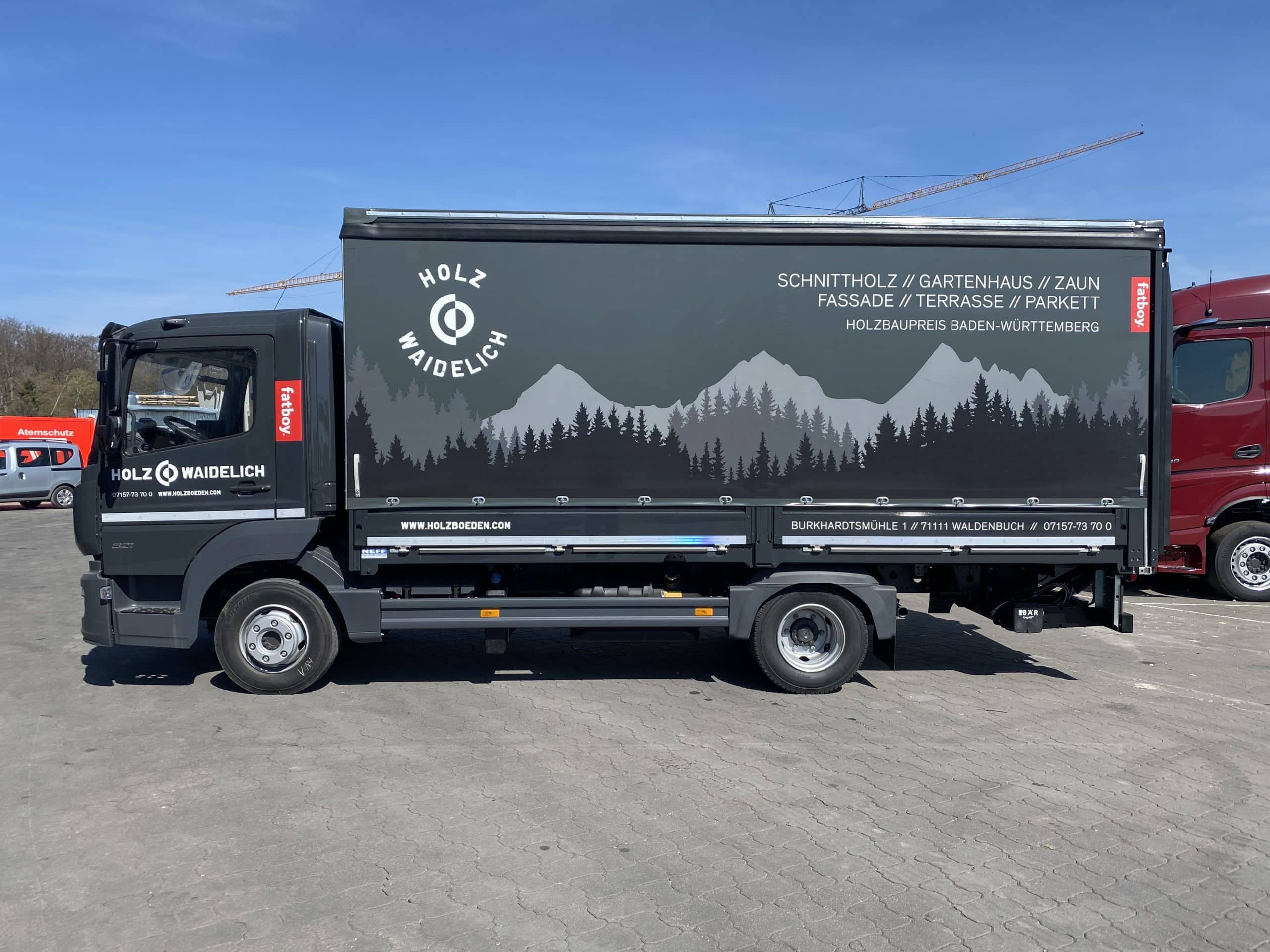 Schwarz folierter Lkw mit Bergsilhouette und Holz-Werbung